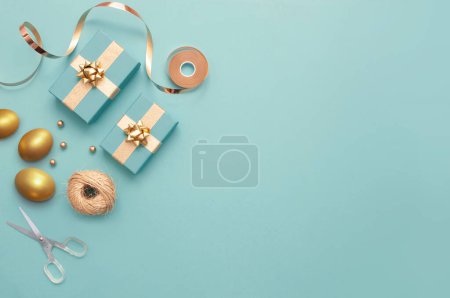 Photo for Top view of easter gift boxes wrapped in gold with gold eggs, and wrapping accessories - Royalty Free Image
