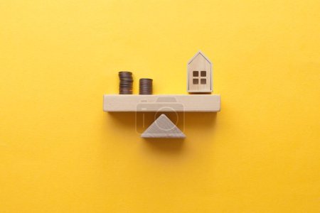 Foto de Casa y monedas equilibradas en un balancín, la inversión inmobiliaria y el concepto de préstamo hipotecario - Imagen libre de derechos