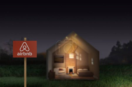 Photo for Airbnb sign next to a model house in the evening with lights on inside in a generic landscape - Royalty Free Image