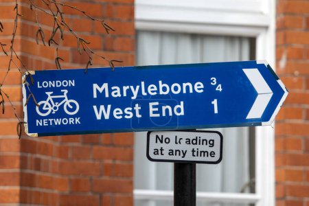 Primer plano de una señal de dirección para ciclistas que muestra la dirección y el kilometraje de Marylebone y el West End en Londres, Reino Unido.