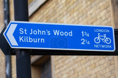 Primer plano de una señal de dirección para ciclistas que muestra la dirección y el kilometraje de St. John 's Wood y Kilburn en Londres, Reino Unido.