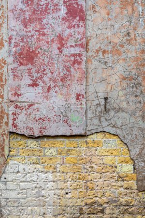 Close-up of peeling plaster and paint revealing the brickwork underneath.