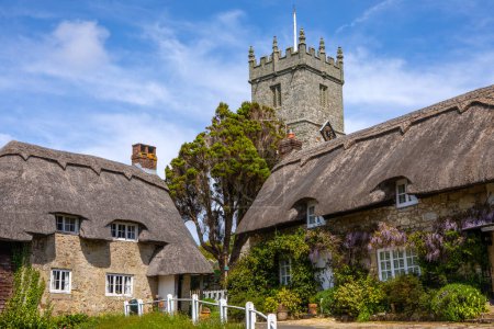 Der Turm der Allerheiligen-Kirche und schöne reetgedeckte Häuschen im malerischen Dorf Godshill auf der Isle of Wight, Großbritannien.