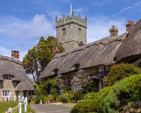 The tower of All Saints Church and beautiful thatched cottages in the picturesque village of Godshill on the Isle of Wight, UK.