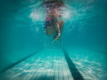 Téléchargez les photos : Une nageuse talentueuse plonge dans une piscine de tournoi pleine grandeur pour s'entraîner ou concourir. - en image libre de droit