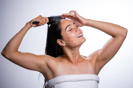Foto de Una joven impresionante cuida su piel y cepilla el cabello con una rutina diaria. Filmada en un estudio sobre un fondo blanco, su belleza natural irradia. - Imagen libre de derechos