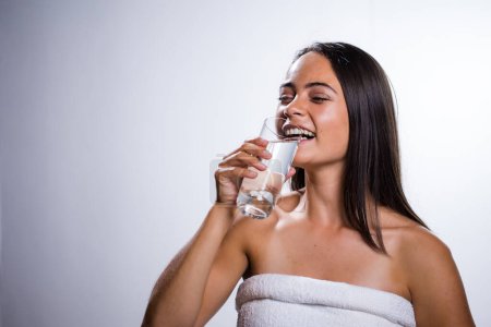 Photo for A beautiful young woman takes a moment to hydrate with water. Shot in a studio on a white background, her natural beauty radiates. - Royalty Free Image