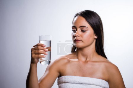 Téléchargez les photos : Une belle jeune femme prend un moment pour s'hydrater avec de l'eau. Tournée dans un studio sur fond blanc, sa beauté naturelle rayonne. - en image libre de droit