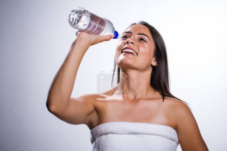 Téléchargez les photos : Une belle jeune femme prend un moment pour s'hydrater avec de l'eau. Tournée dans un studio sur fond blanc, sa beauté naturelle rayonne. - en image libre de droit