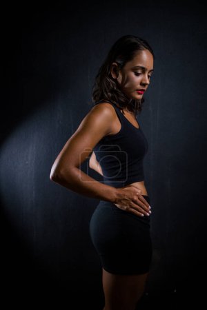 Téléchargez les photos : Jolie fille brune posant pour une séance photo de fitness dans un studio. Elle est vêtue d'un short serré et d'un haut de culture, et ses poses véhiculent un sentiment de force, d'athlétisme et de forme physique.. - en image libre de droit