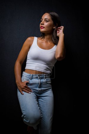 Photo for Pretty dark haired girl posing for a fashion shoot in a studio. She is dressed in stylish jeans and a crop top, and her poses convey a sense of youthfulness and vitality. - Royalty Free Image