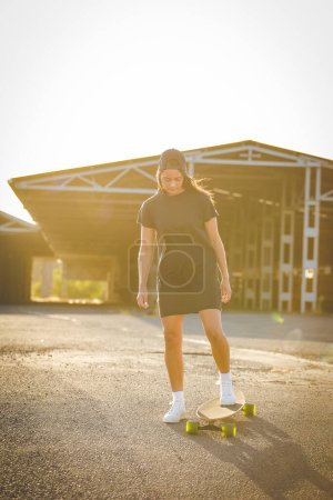 Téléchargez les photos : Jolie jeune femme aux cheveux foncés skateboard dans un environnement urbain dynamique. - en image libre de droit