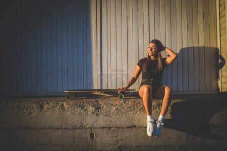 Foto de Bonita mujer joven con el monopatín pelo oscuro en un entorno urbano vibrante. - Imagen libre de derechos