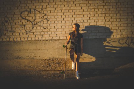 Téléchargez les photos : Jolie jeune femme aux cheveux foncés skateboard dans un environnement urbain dynamique. - en image libre de droit
