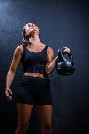 Photo for Pretty dark haired girl posing with a kettle bell for a fitness photo shoot in a studio. - Royalty Free Image