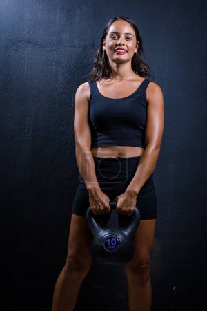 Téléchargez les photos : Jolie fille brune posant avec une cloche de bouilloire pour une séance photo de fitness dans un studio. - en image libre de droit