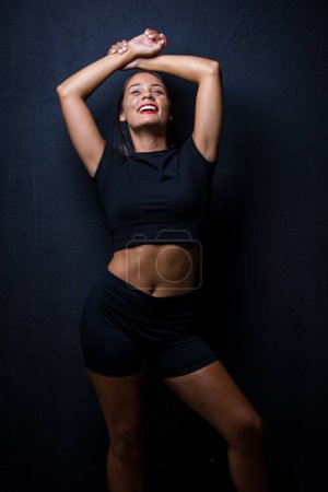 Photo for Pretty dark haired girl posing for a fitness photo shoot in a studio. She is dressed in tight shorts and a crop top, and her poses convey a sense of strength, athleticism, and fitness. - Royalty Free Image