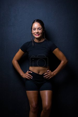 Photo for Pretty dark haired girl posing for a fitness photo shoot in a studio. She is dressed in tight shorts and a crop top, and her poses convey a sense of strength, athleticism, and fitness. - Royalty Free Image