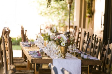 Dieses fesselnde Bild zeigt das elegante Dekor und die atemberaubenden Blumenarrangements einer echten Hochzeit. Das Foto zeigt einen wunderschön dekorierten Tisch in einer charmanten Hochzeitslocation, geschmückt mit zarten Blumen, Kerzen und anderen dekorativen Elementen.