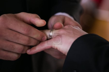 Foto de Esta hermosa imagen captura el momento íntimo de una pareja intercambiando anillos de boda en una boda real. La fotografía muestra un primer plano de las manos de la pareja, mostrando sus dedos entrelazados y las bandas de boda en sus dedos. La imagen - Imagen libre de derechos