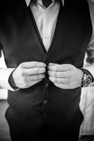 This captivating image showcases the groom's wedding attire, including his suit, shoes, and cufflinks, as he gets dressed for his big day. The photograph highlights the intricate details of the groom's ensemble, creating a beautiful composition that 
