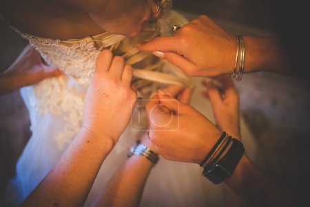Photo for A touching moment captured as the bride is getting dressed, helped by her family members, putting on her shoes and garter, and having her dress closed in anticipation of her big day. - Royalty Free Image
