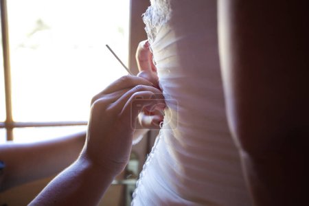 Photo for A touching moment captured as the bride is getting dressed, helped by her family members, putting on her shoes and garter, and having her dress closed in anticipation of her big day. - Royalty Free Image