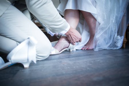Foto de Un momento conmovedor capturado mientras la novia se viste, ayudada por los miembros de su familia, poniéndose los zapatos y la liga, y teniendo su vestido cerrado en anticipación de su gran día. - Imagen libre de derechos