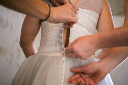 A touching moment captured as the bride is getting dressed, helped by her family members, putting on her shoes and garter, and having her dress closed in anticipation of her big day.