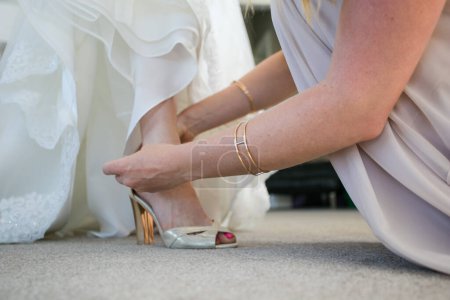 Foto de Un momento conmovedor capturado mientras la novia se viste, ayudada por los miembros de su familia, poniéndose los zapatos y la liga, y teniendo su vestido cerrado en anticipación de su gran día. - Imagen libre de derechos