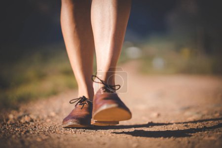 Photo for Close up image of a pretty woman with muscular legs walking on a dirt road wearing handmade leather shoes. - Royalty Free Image