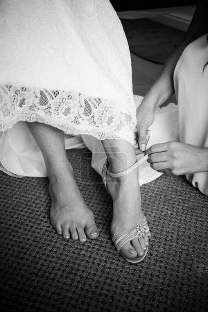 Téléchargez les photos : Un moment touchant capturé alors que la mariée s'habille, aidée par les membres de sa famille, enfilant ses chaussures et sa jarretière, et ayant sa robe fermée en prévision de son grand jour. - en image libre de droit