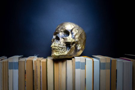 Human Skull gold on books dark background