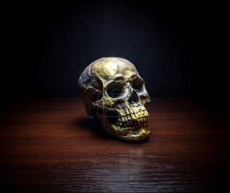 Foto de Calavera humana vista lateral de oro mesa de madera fondo oscuro - Imagen libre de derechos