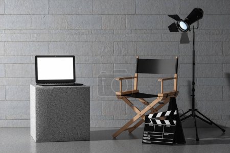 Photo for Modern Laptop with Blank Screen near Director Chair, Movie Clapper and Spotlight in front of stone blocks wall background. 3d Rendering - Royalty Free Image