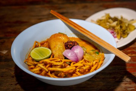 Foto de Khao Soi, Khao Soi Kai, fideos tailandeses Khao Soi, pollo al curry con condimentos en suelo de madera, concepto de comida tailandesa del norte. (Lanna comida) - Imagen libre de derechos