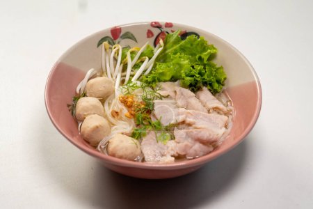 Photo for Hand holding chopsticks and eating rice noodle soup with pork, pork ball and vegetables in a bowl, Thai noodles soup - Royalty Free Image