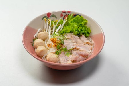 Ręczne trzymanie pałeczek i jedzenie zupy z makaronem ryżowym z wieprzowiną, kulą wieprzową i warzywami w misce, zupa z tajskiego makaronu