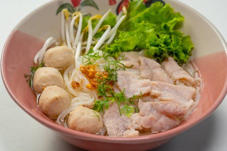 Ręczne trzymanie pałeczek i jedzenie zupy z makaronem ryżowym z wieprzowiną, kulą wieprzową i warzywami w misce, zupa z tajskiego makaronu