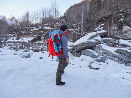 Foto de Popular invierno actividades al aire libre. Senderismo masculino con mochila y bastones nórdicos en la nieve. - Imagen libre de derechos
