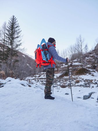 Foto de Popular invierno actividades al aire libre. Senderismo masculino con mochila y bastones nórdicos en la nieve. - Imagen libre de derechos