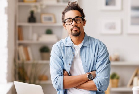 Téléchargez les photos : Portrait d'un homme entrepreneur afro-américain sérieux portant des lunettes et les cheveux longs regardant la caméra au bureau à domicile sur fond flou - en image libre de droit