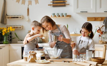 Foto de Madre amante del contenido y niños lindos: hijo e hija agregando ingredientes en el tazón y preparando la masa en la mesa en casa - Imagen libre de derechos