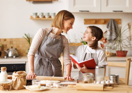 Foto de Joven mujer sonriente madre haciendo galletas de masa con linda hijita mientras están de pie juntos en la cocina en casa, - Imagen libre de derechos