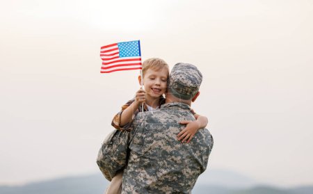 Photo for Happy little boy son with American flag hugging father in military uniform came back from US army, rear view of male soldier reunited with family while standing in green meadow on summer day - Royalty Free Image