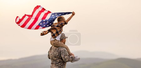 Foto de Militar padre llevando feliz hijo pequeño con bandera americana en hombros y disfrutando de la increíble vista de la naturaleza de verano en el día soleado el 4 de julio, feliz padre soldado masculino se reunió con el hijo después del ejército de EE.UU. - Imagen libre de derechos