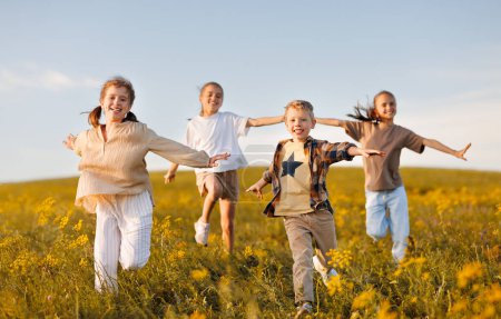Téléchargez les photos : Groupe de joyeux écoliers joyeux courir avec les bras tendus dans le champ le jour ensoleillé du printemps, les enfants excités garçons et filles profitant des vacances d'été à la campagne - en image libre de droit
