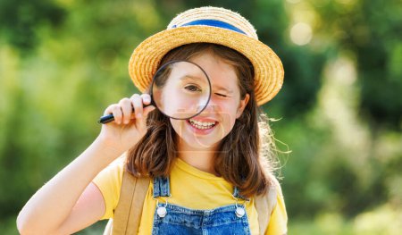 Photo for Cheerful happy girl with magnifying glass in her hands studies the environment in summer in nature - Royalty Free Image