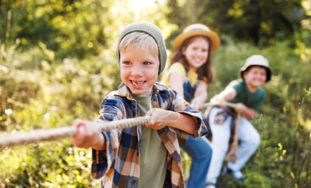 Téléchargez les photos : Groupe d'enfants joyeux jouer à l'extérieur, remorqueur de guerre en été à l'extérieur - en image libre de droit