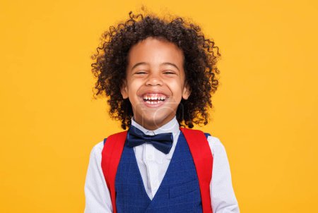 Foto de Deleitado niño afroamericano estudiante se ríe de la cámara mientras se divierte durante la escuela contra el fondo amarillo - Imagen libre de derechos